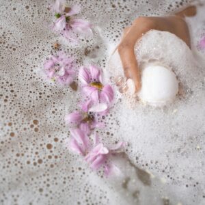 A calming spa scene with a hand holding a bath bomb amidst pink flower petals.